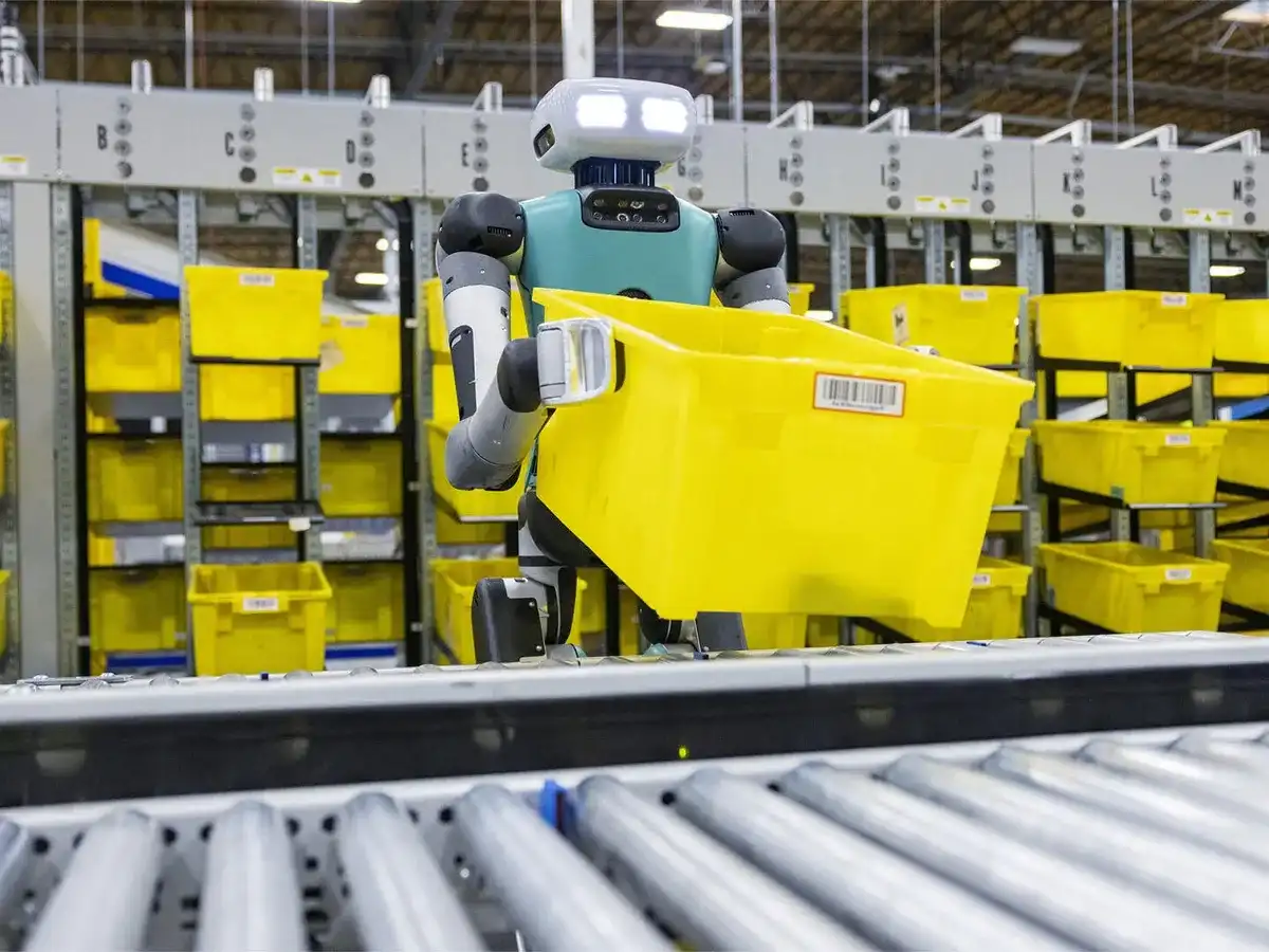 Autonomous Amazon robot carrying a yellow storage container along a warehouse conveyor system.