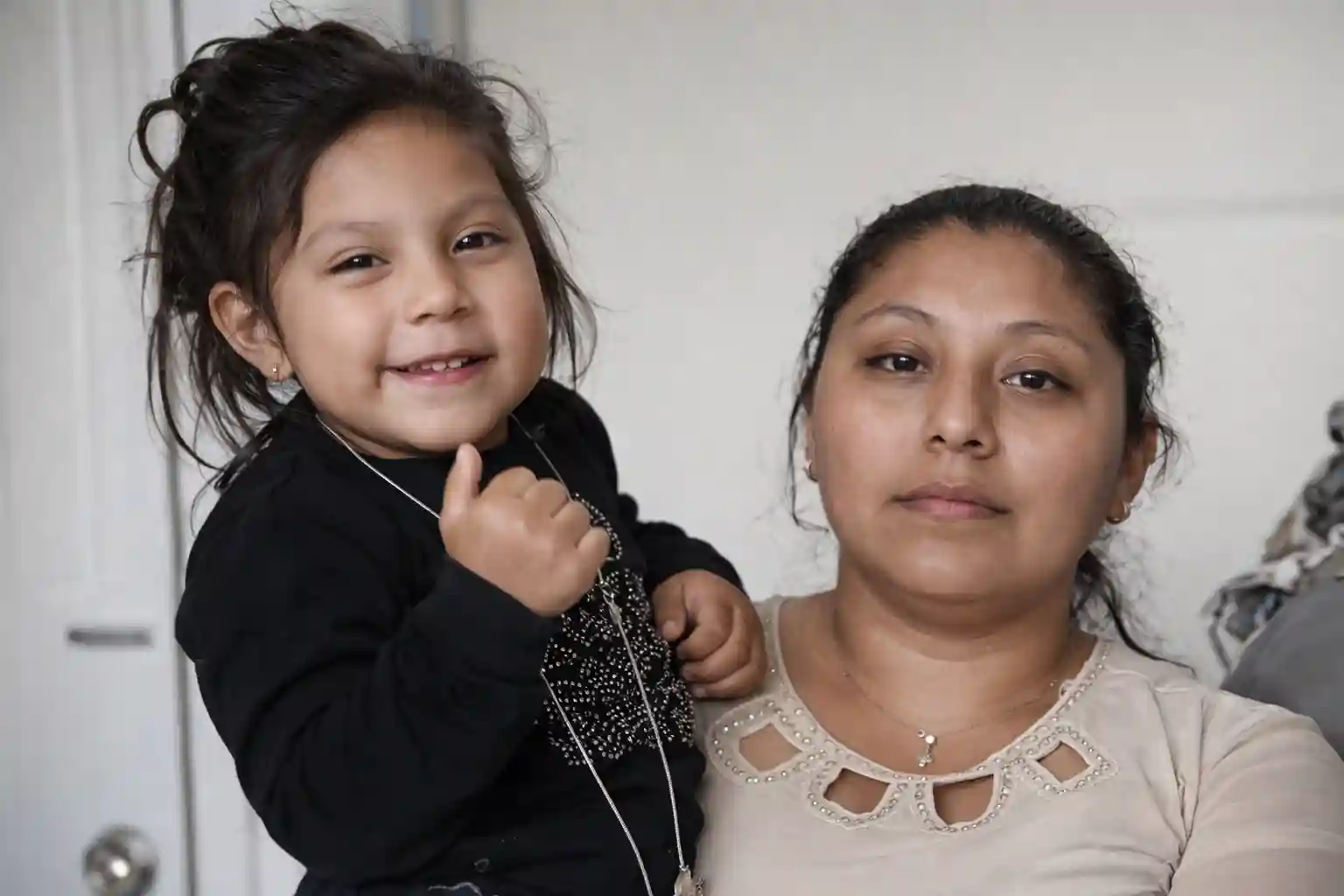Woman holding a smiling young girl indoors, both facing the camera