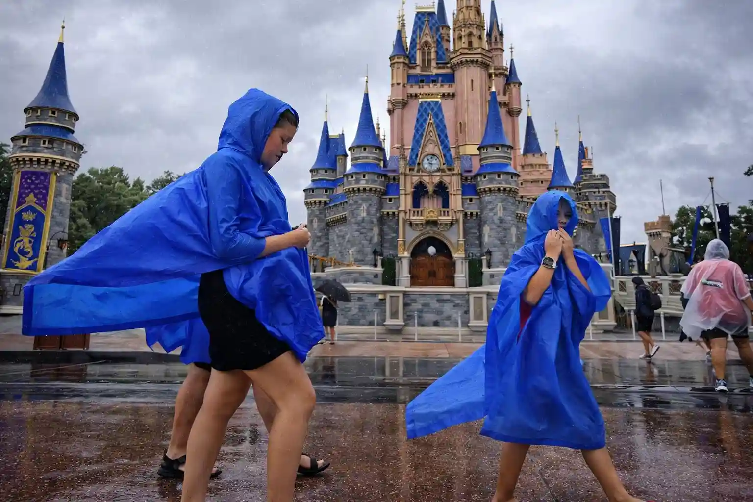 Visitors in blue ponchos walking through Disney World's Magic Kingdom during rainy weather, with Cinderella Castle in the background