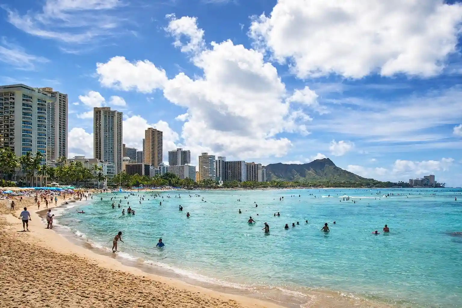 Waikiki Beach, Honolulu with tourists swimming and iconic skyscrapers.