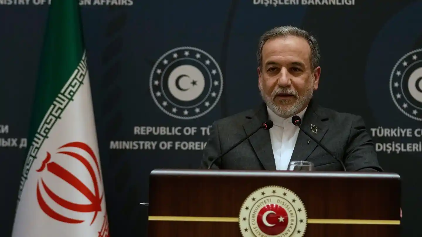 Image of an Iranian diplomat giving a press conference with flags of Iran and Turkey in the background.