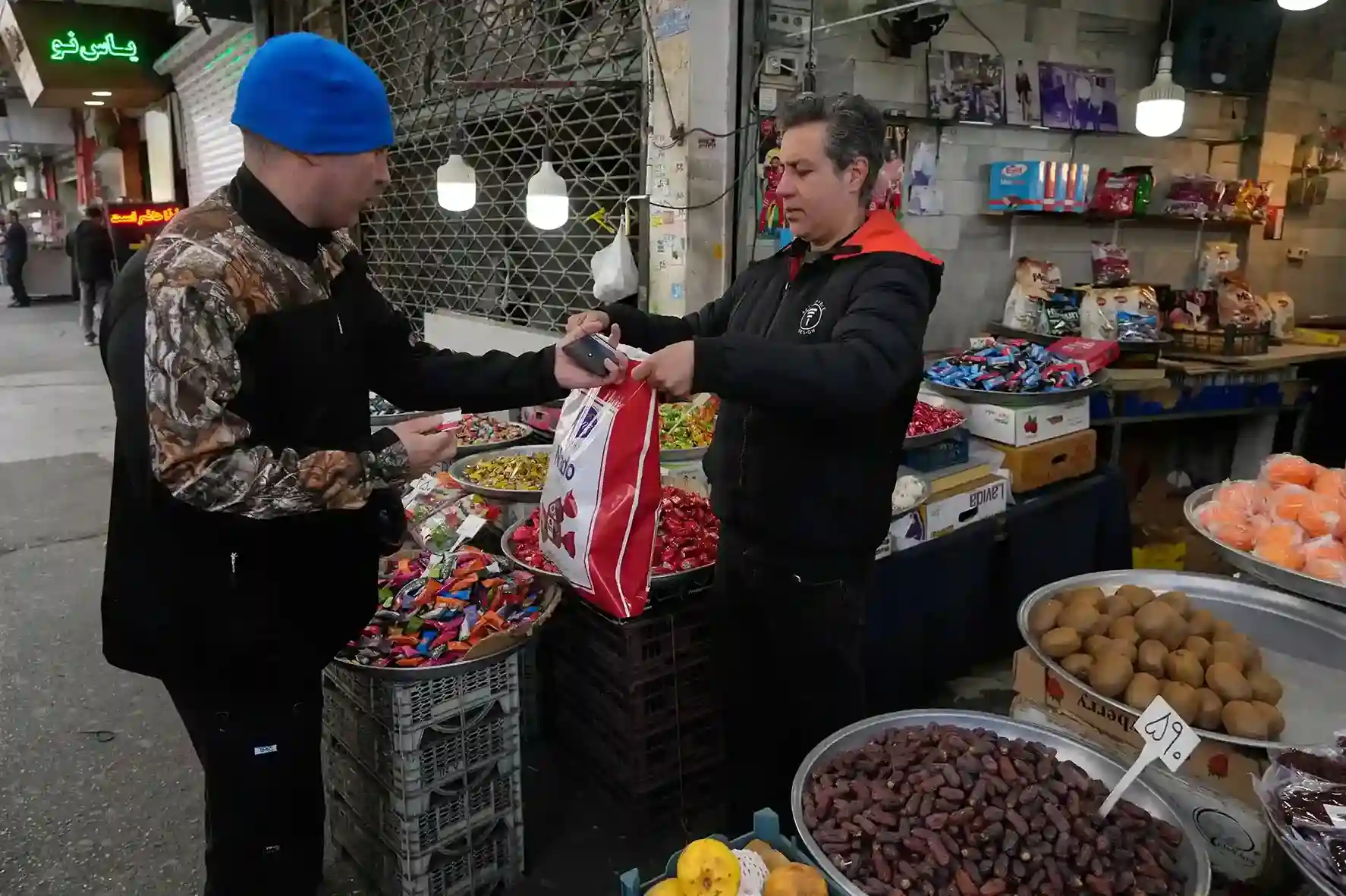 Local street vendor selling candy and dates to a customer at a traditional market in Iran