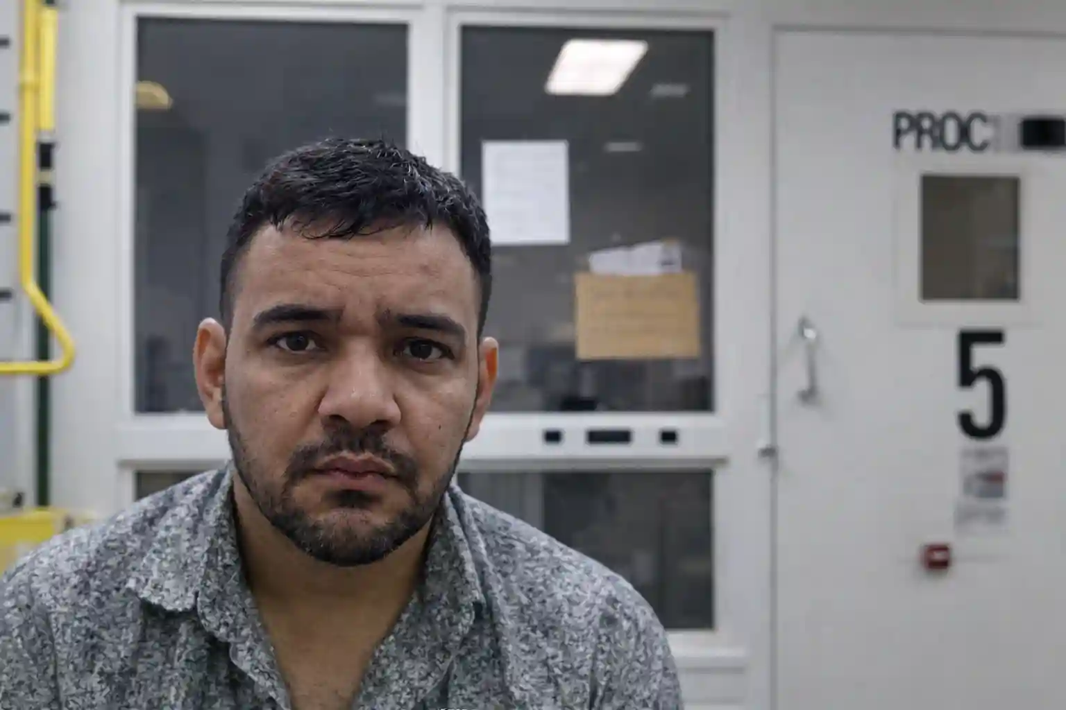 Man seated inside a federal processing facility, facing the camera during immigration custody processing.
