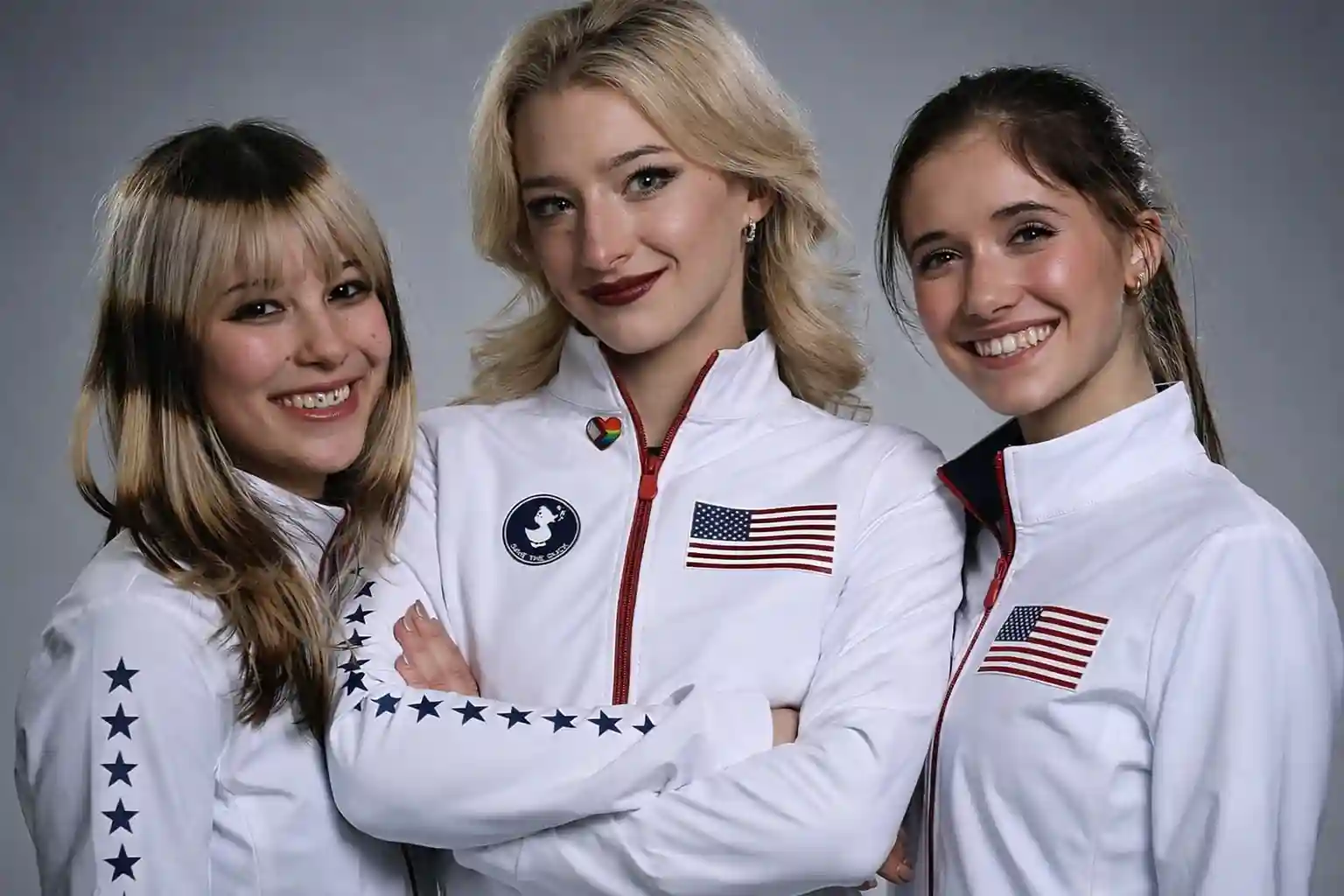 Three Team USA women figure skaters pose together in white Olympic jackets.