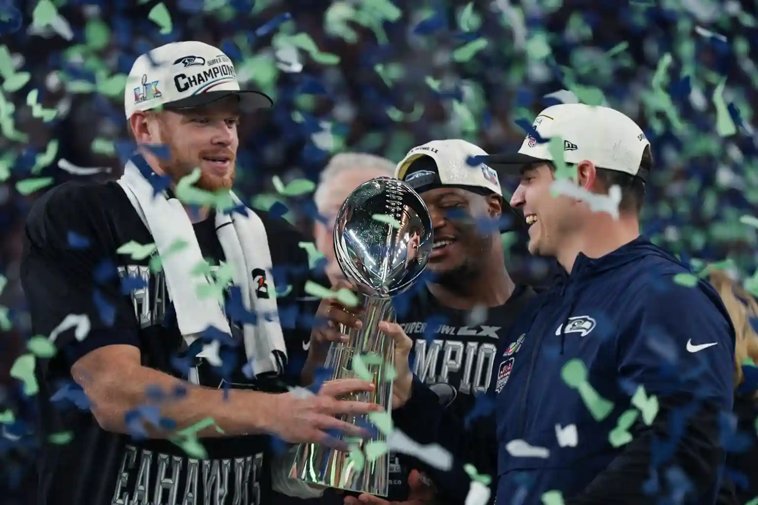 Seattle Seahawks players celebrating with the Vince Lombardi Trophy after winning Super Bowl 60, confetti raining down.