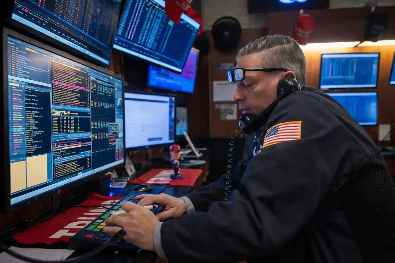 Stock trader at his desk, speaking on the phone, analyzing data across multiple screens.