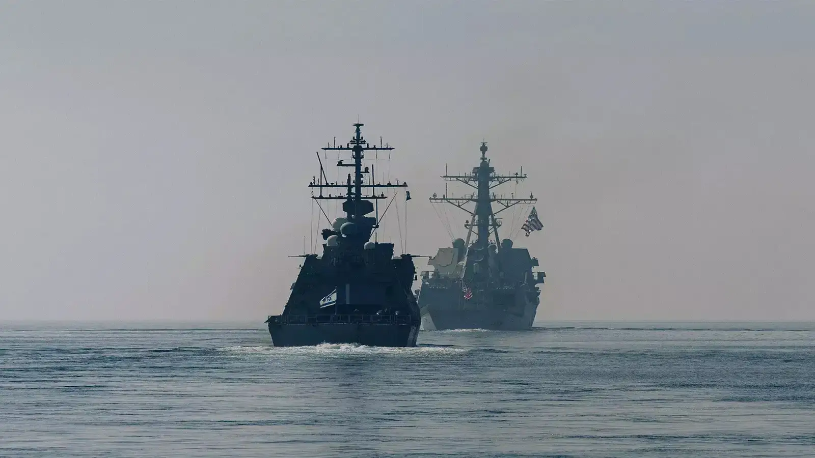 US Navy destroyers sailing through the Arabian Sea with a clear view of their radar masts and American flags.