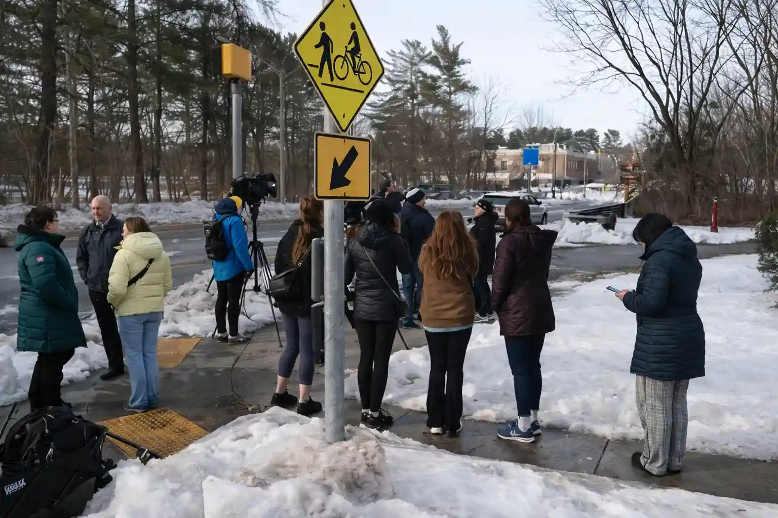 Media crews and community members gathered on a snowy sidewalk near an intersection outside Thomas S. Wootton High School following the shooting incident
